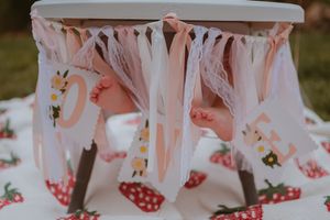 Pink party decorations and streamers attached to a white table, set against a blurred outdoor background.