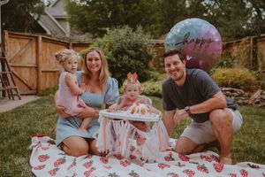 Family enjoying a picnic together outdoors on a colorful blanket with snacks and drinks on a sunny day.