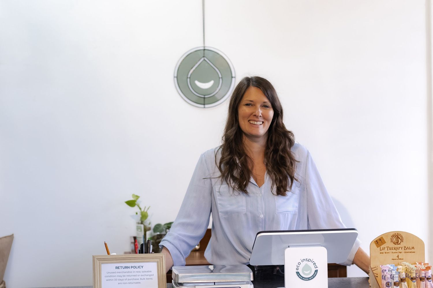 Smiling entrepreneur works at desk with laptop and office supplies while standing in bright workspace with wall clock.