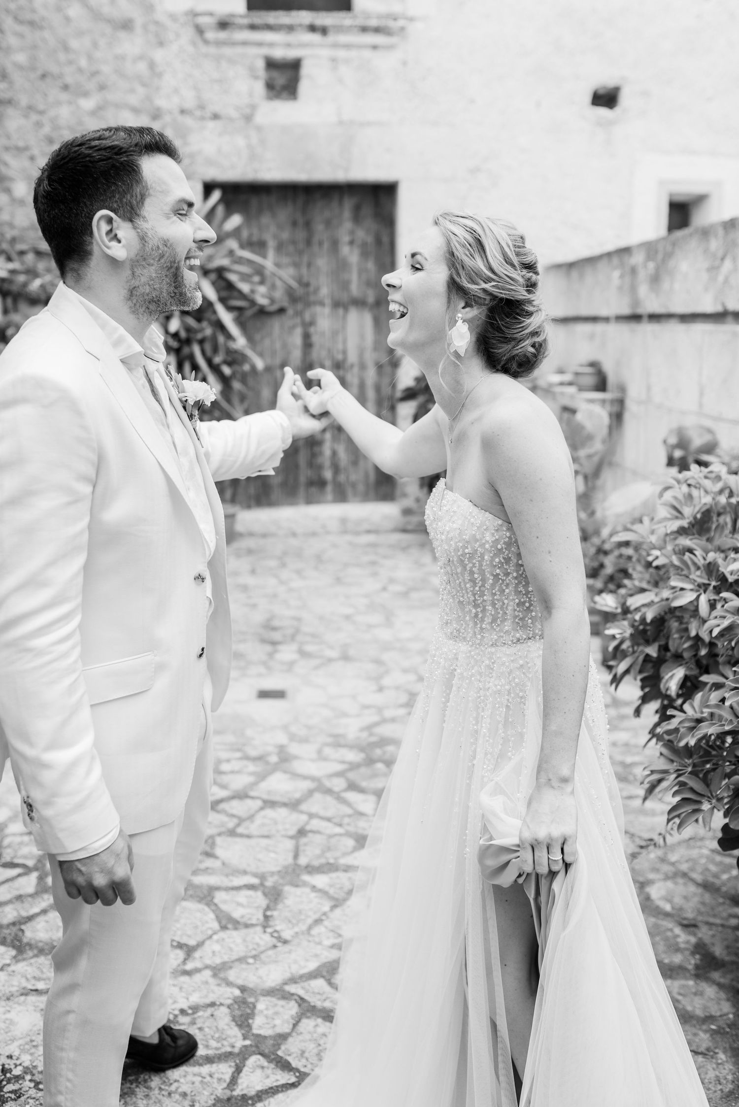 Schwarz-Weiß-Foto eines lachenden Hochzeitspaares, das gemeinsam einen freudigen Moment auf einer mallorquinischen Steinterrasse verbringt.