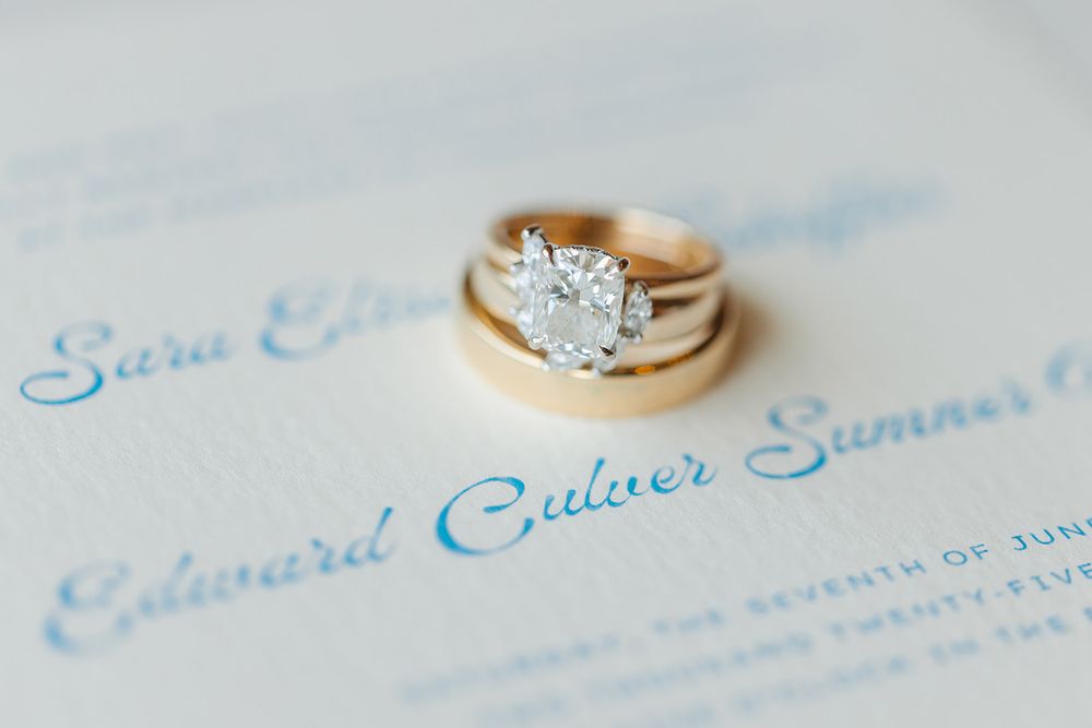 Diamond engagement ring sparkles against wedding invitation text on soft white background.