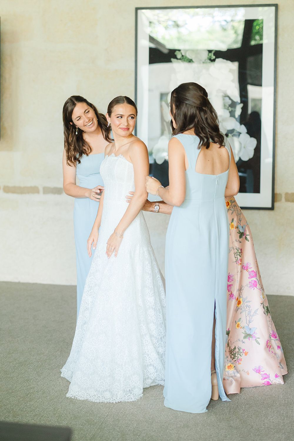 Wedding party gathering indoors with bride in white lace gown and bridesmaids in light blue dresses.
