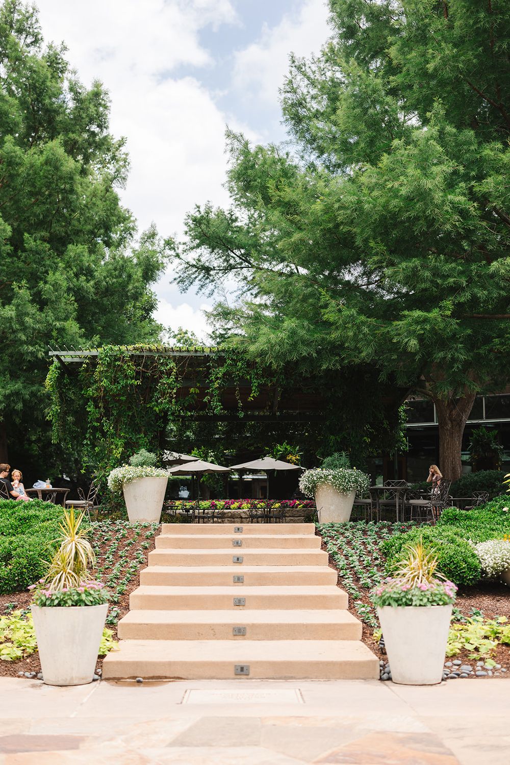 A beautiful garden patio with stone steps, large white planters, and decorative string lights under a canopy of trees.