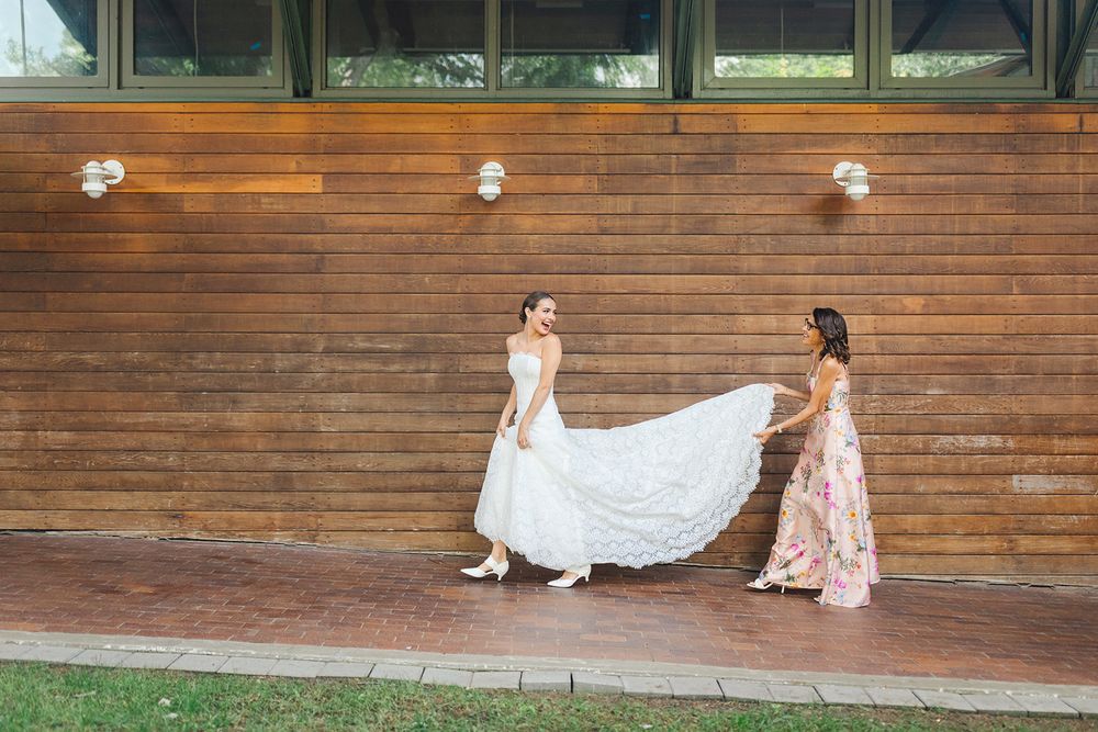 Pink bridesmaids help adjust the flowing white wedding gown against a rustic wooden wall backdrop.