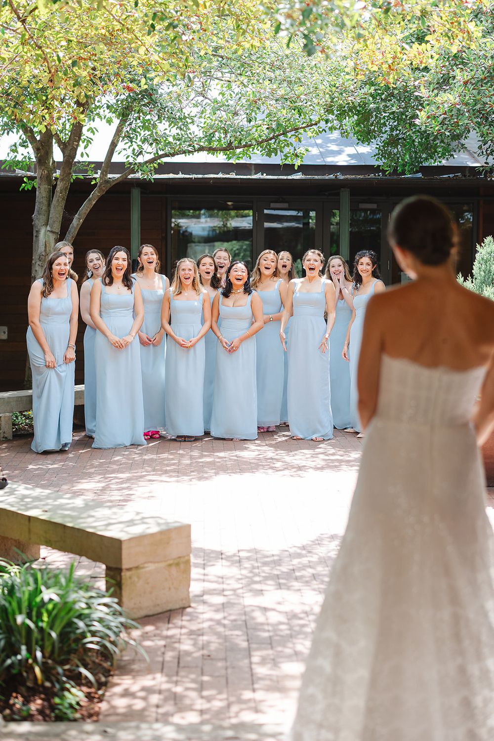 Bridesmaids wearing light blue floor-length dresses gather outdoors for a first look with the bride.