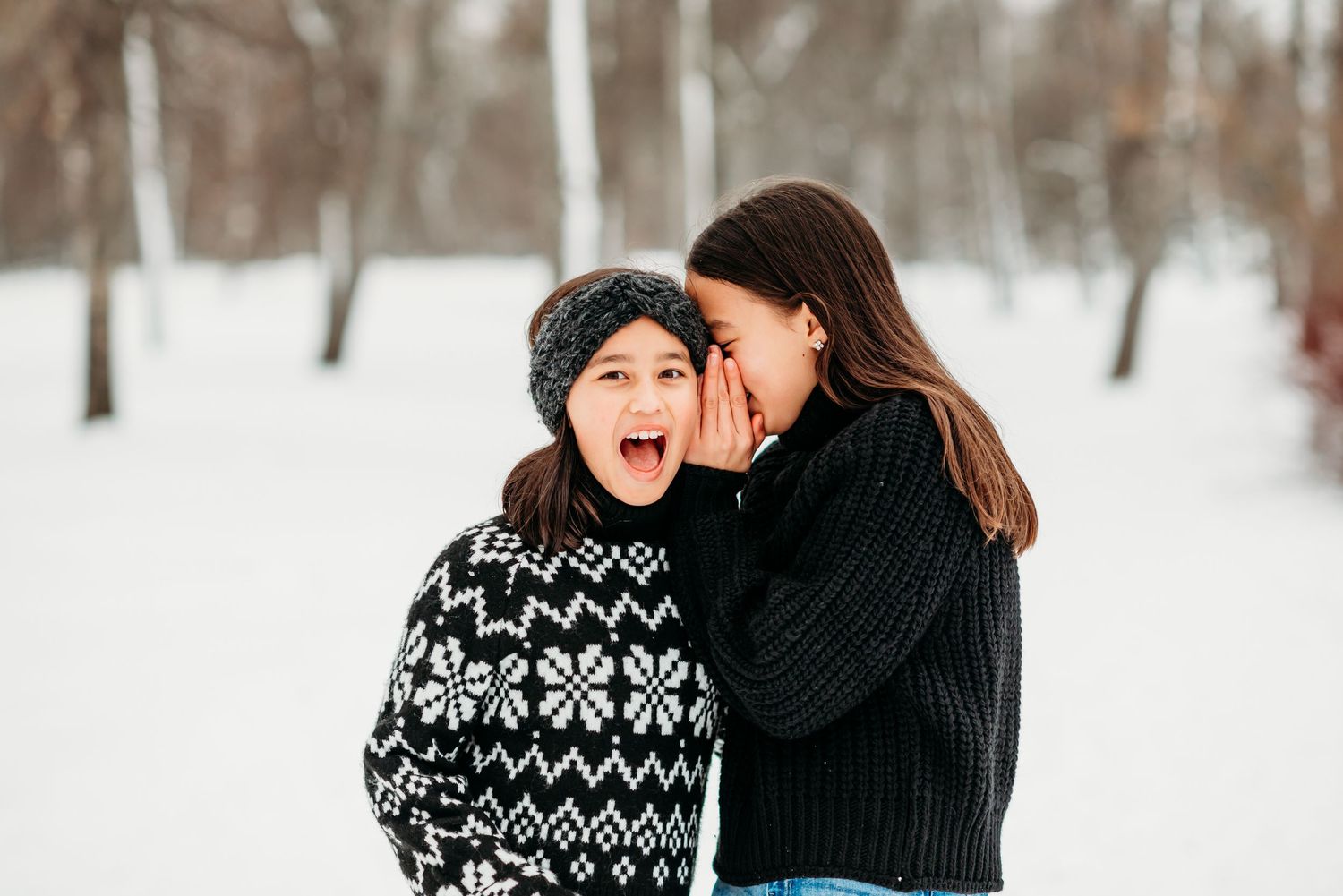 Two people in winter sweaters share joyful moments in a snowy forest setting.