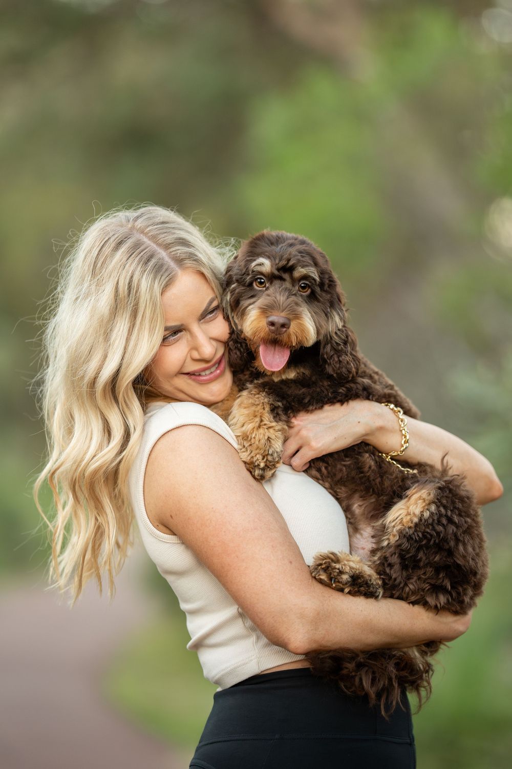 A brown cockapoo puppy being held and cuddled outdoors with a natural green background.