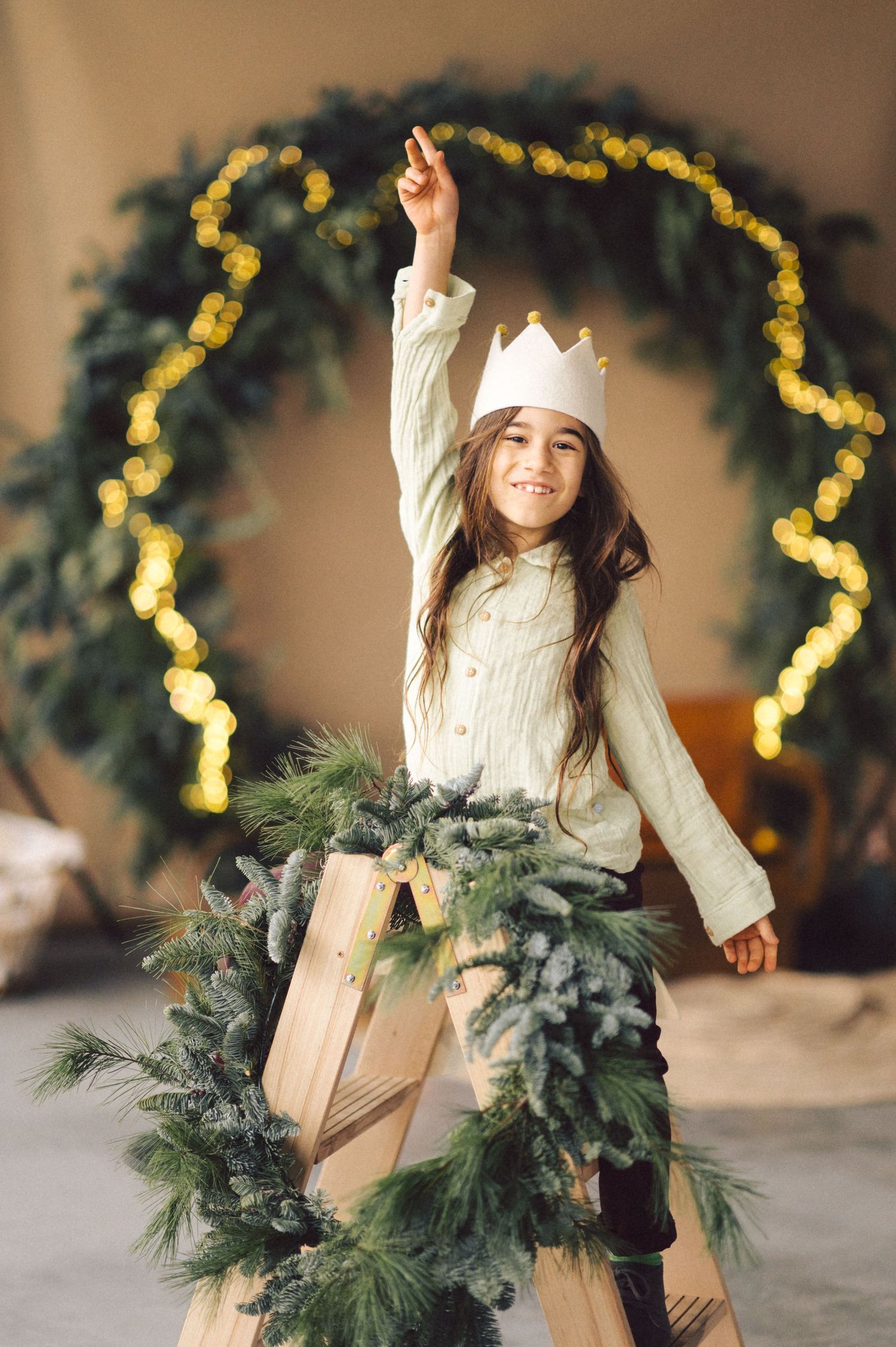Young girl in cream sweater dances near Christmas decorations with pine garland and twinkling lights.