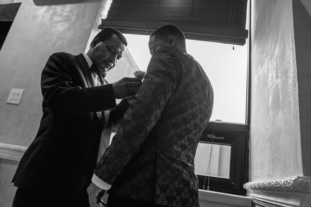 A black and white image shows two men during a formal preparation moment.