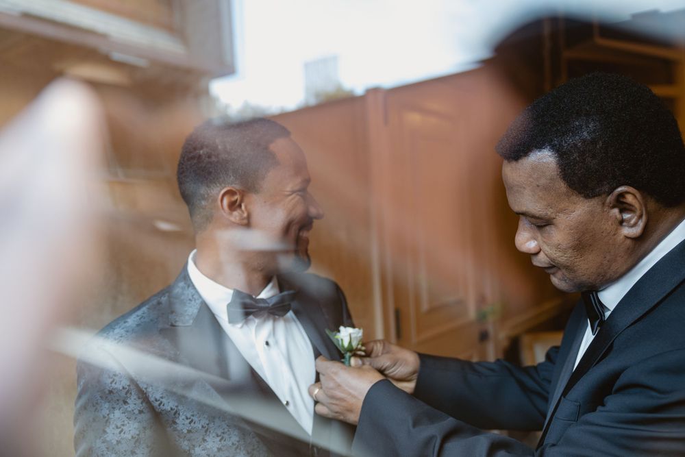 A blurred foreground frames two men in bow ties during a pre-event preparation moment.