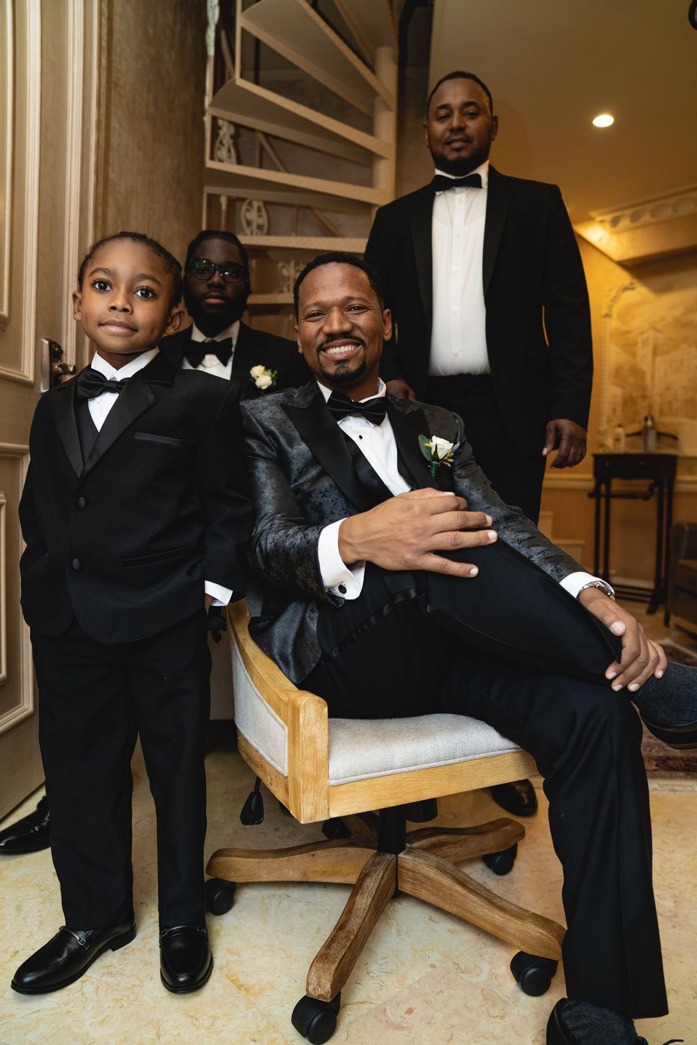 Groomsmen seated together in formal attire with bowties and tuxedos during wedding preparations.