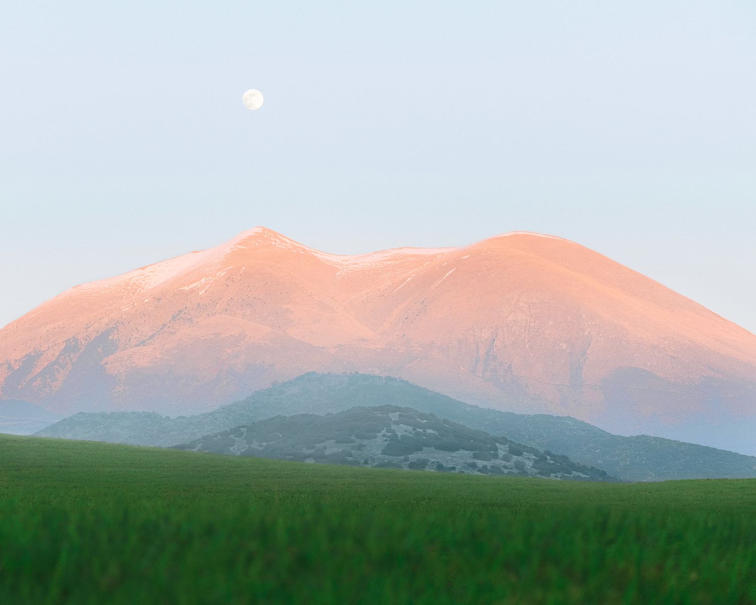 Mount Olympus at sunrise with moon above, seen from green fields