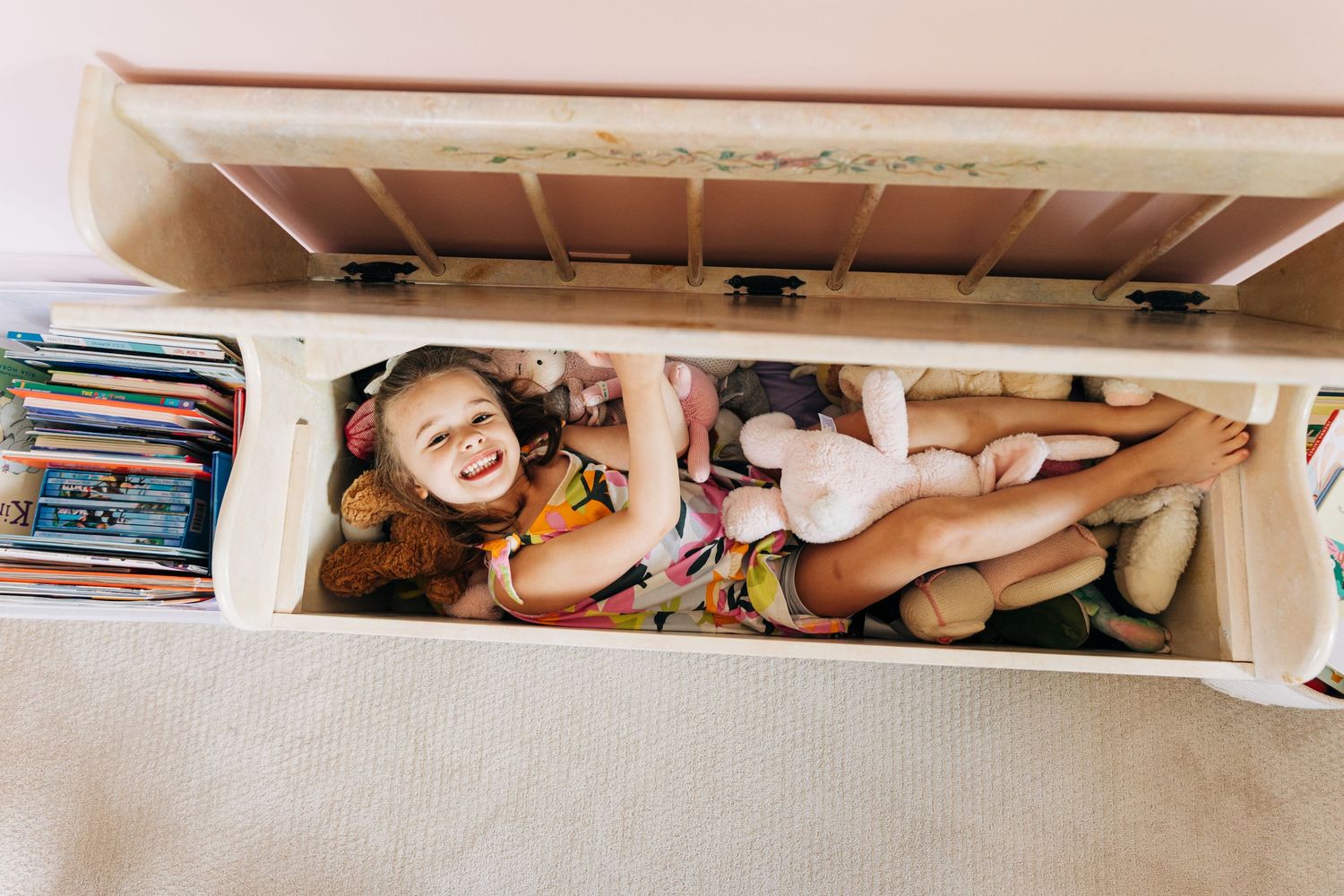 A little girl smiles while hiding in her toy box filled with toys