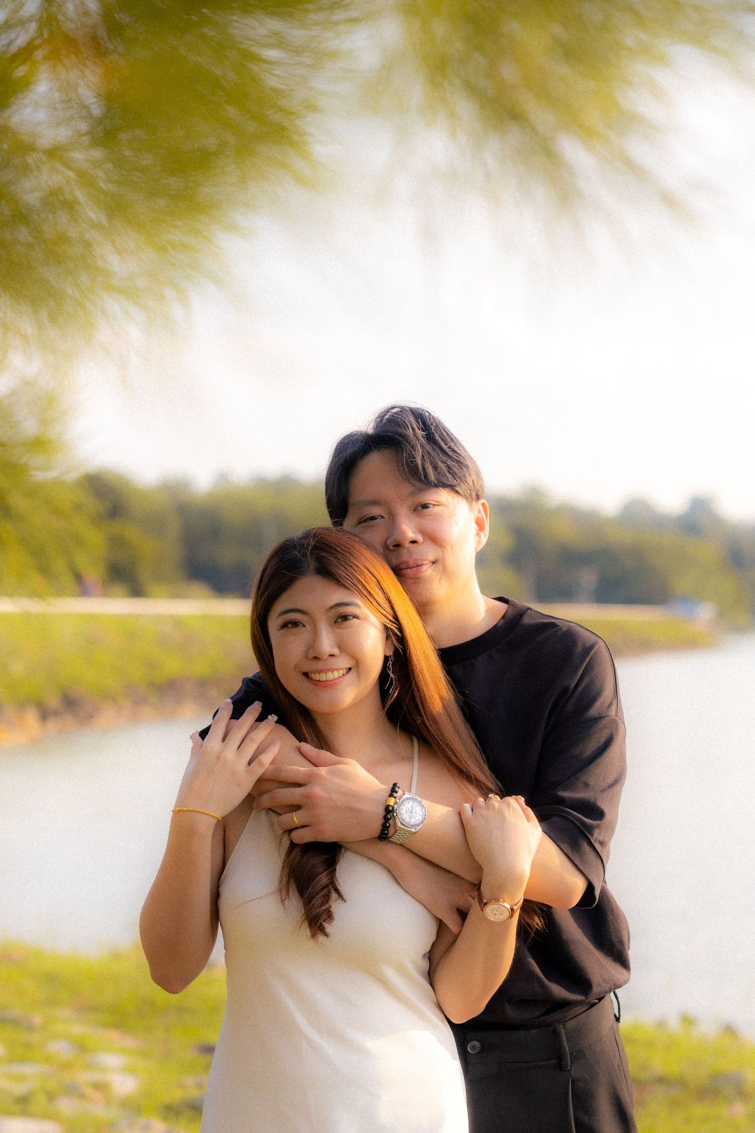A couple shares a romantic moment by a scenic lakeside with golden sunlit trees in the background.