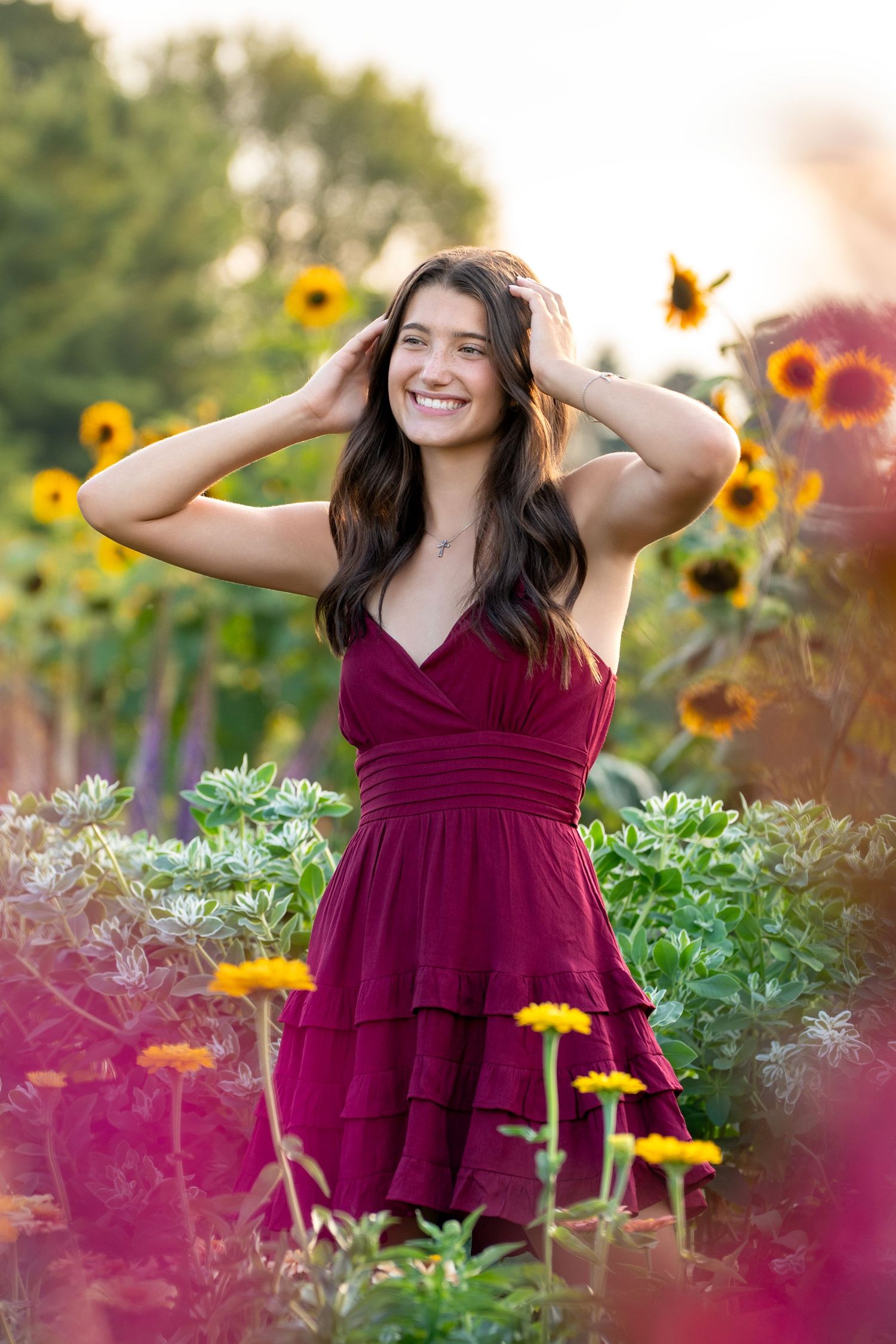 A burgundy dress stands out beautifully against vibrant yellow sunflowers and greenery in a summer garden photo session.