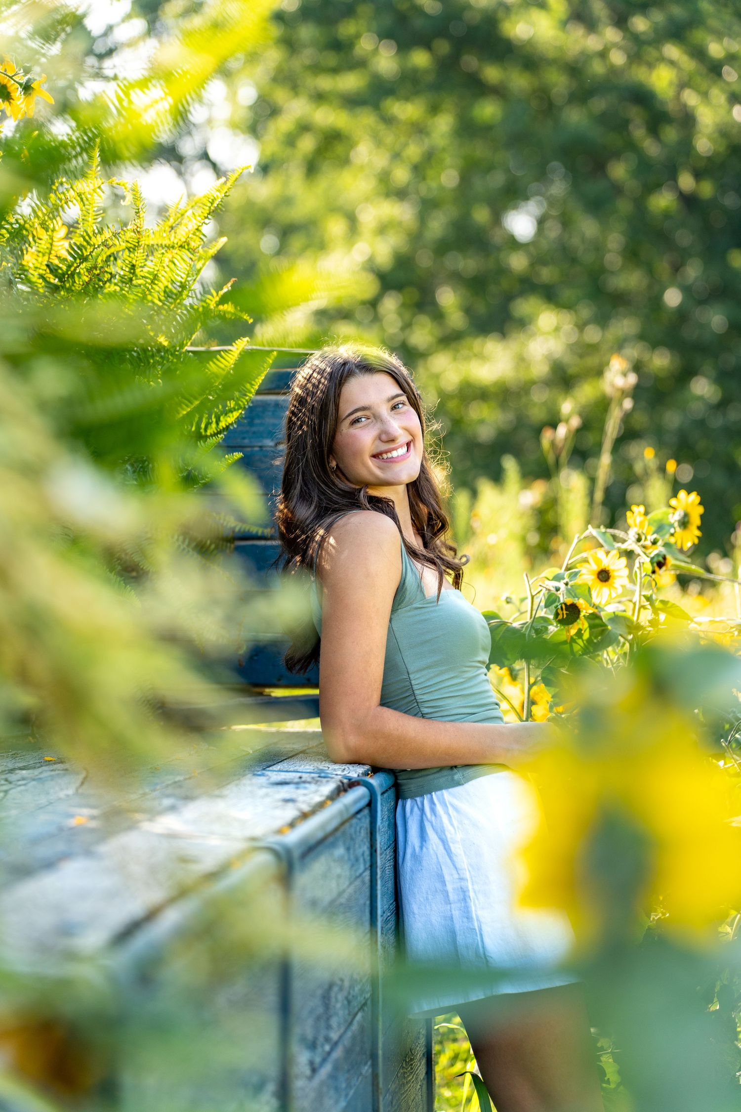 Outdoor portrait in a garden with sunlit yellow flowers and green foliage framing the composition on a sunny summer day.