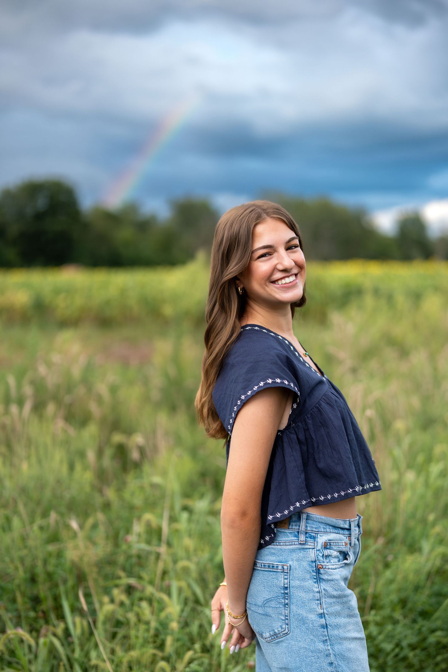 A rainbow appears over green meadows during a summer photoshoot with overalls against stormy clouds.