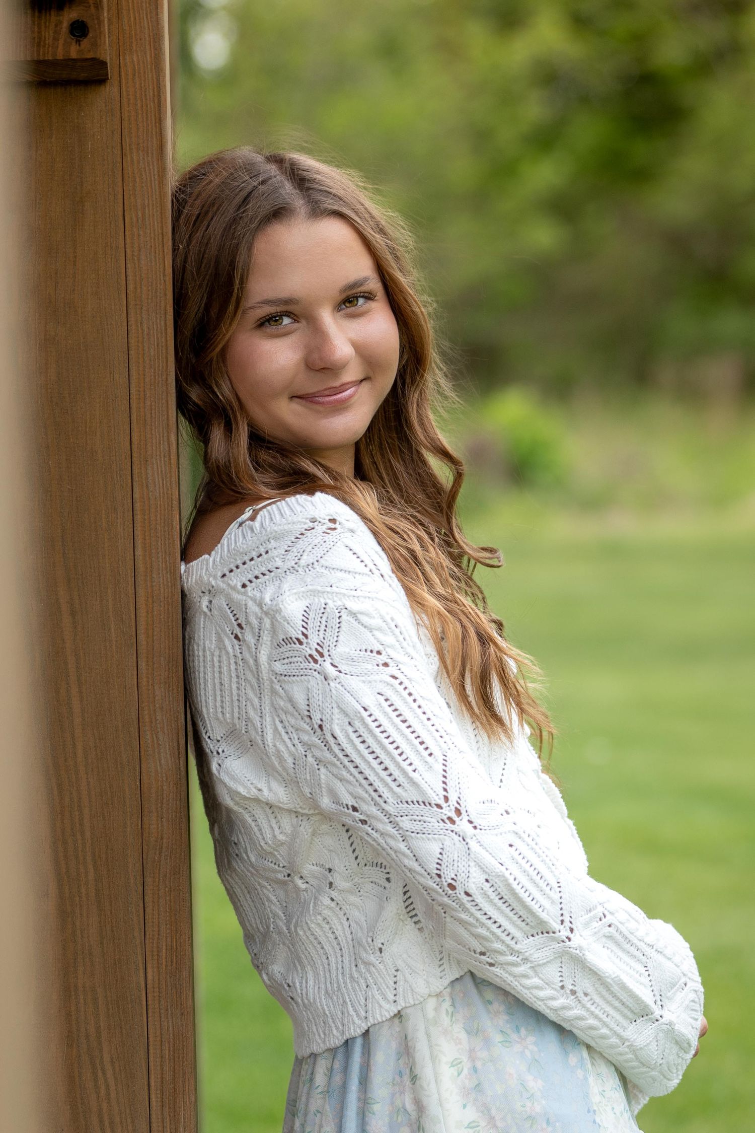 A serene spring portrait in white lace by a wooden post with soft natural bokeh in the background.