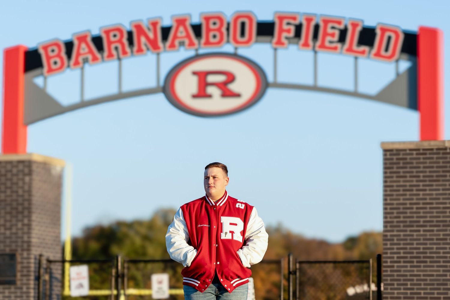 High school varsity baseball team practices on field while red and white stadium signs adorn the outfield fence.