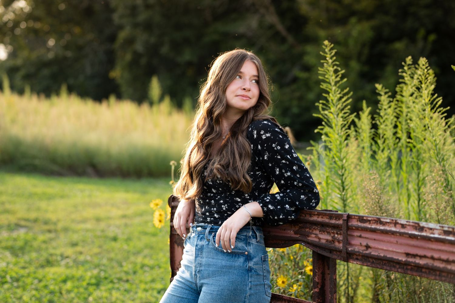 A dreamy outdoor photoshoot featuring someone in denim overalls and a polka dot top in a sunlit field with tall grass.