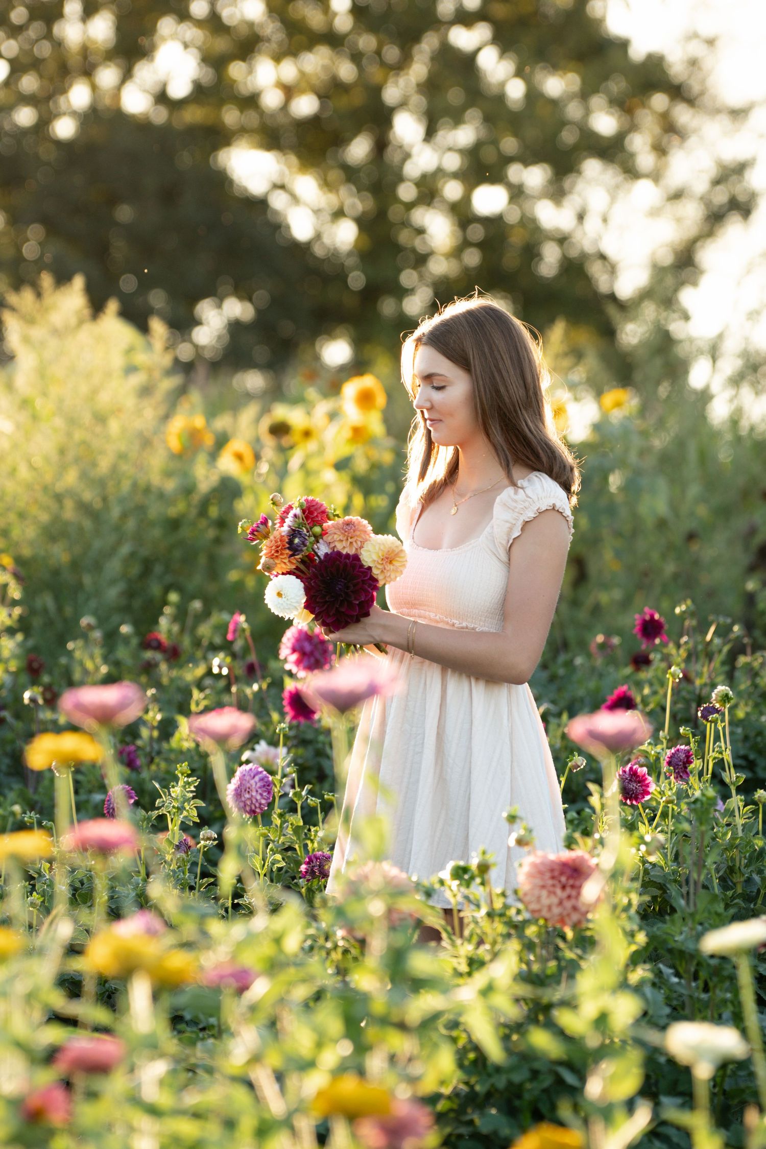 A person in a white dress stands in a colorful wildflower garden gathering blooms at golden hour.