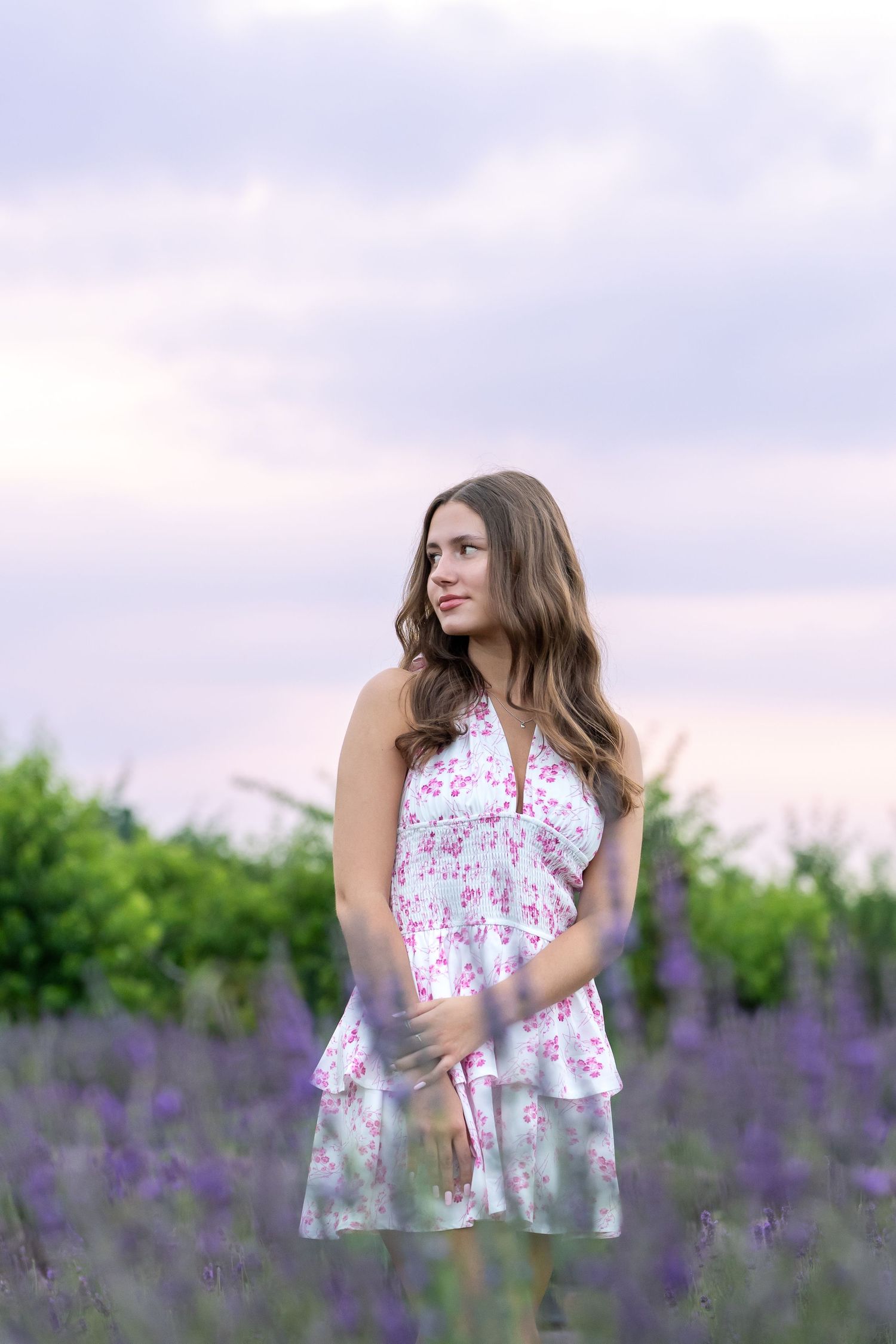 A person in a floral summer dress stands thoughtfully in a blooming lavender field at sunset.