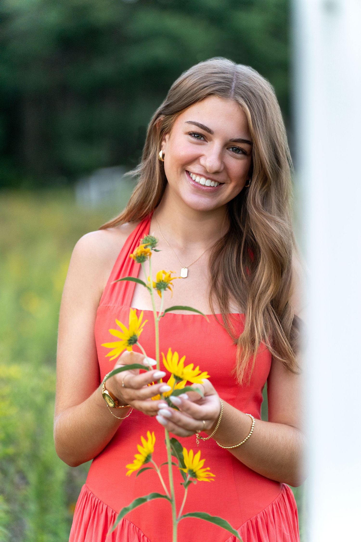 Woman in coral dress poses with yellow sunflowers in outdoor garden setting during summer photo session.