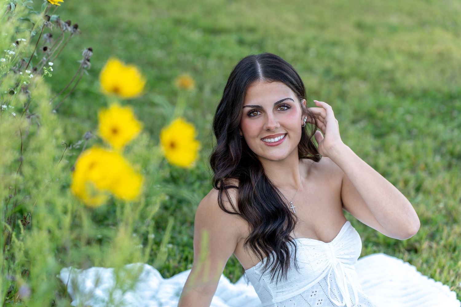 Woman in white dress lying in sunny field with scattered yellow wildflowers on green grass.