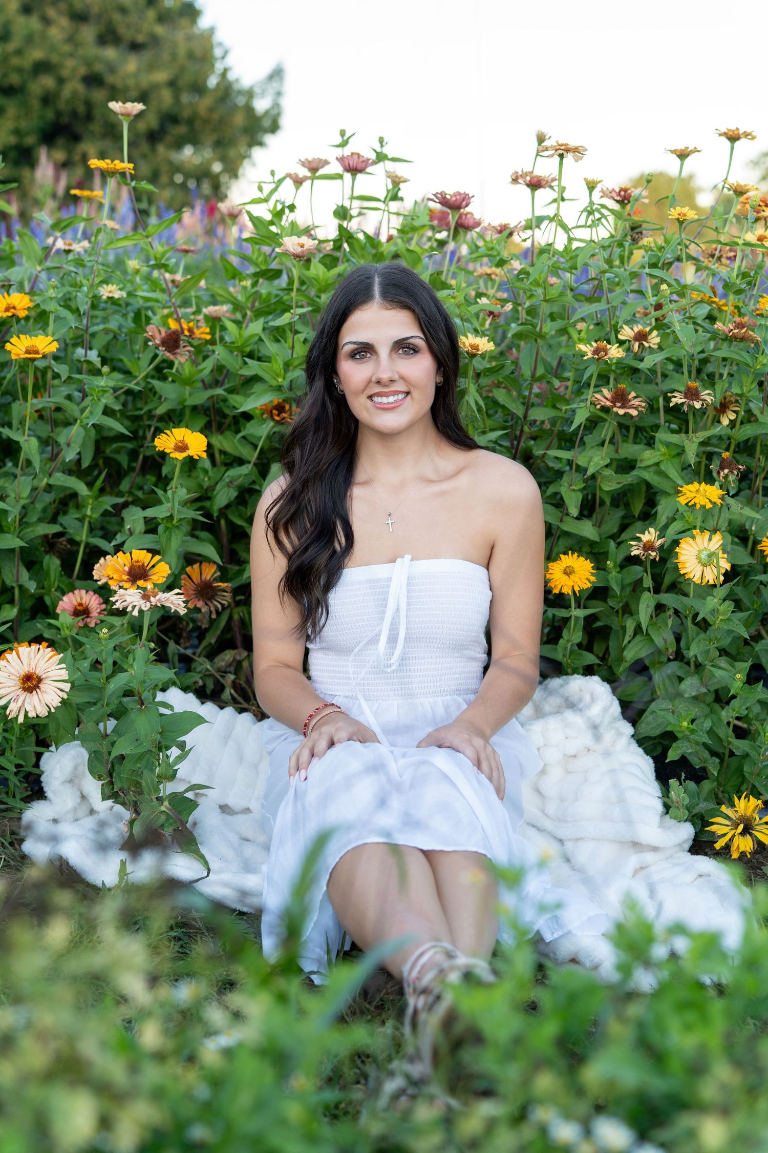 A strapless white dress stands out among vibrant yellow and orange zinnias in a summer garden setting.