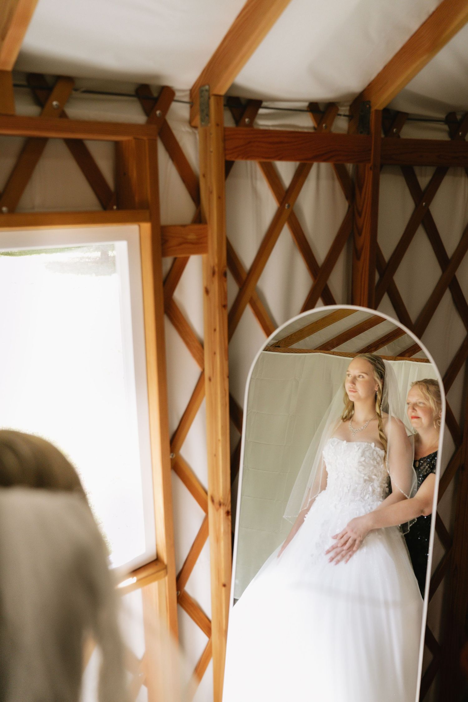 A wedding dress hangs in a rustic wooden room with natural window light.