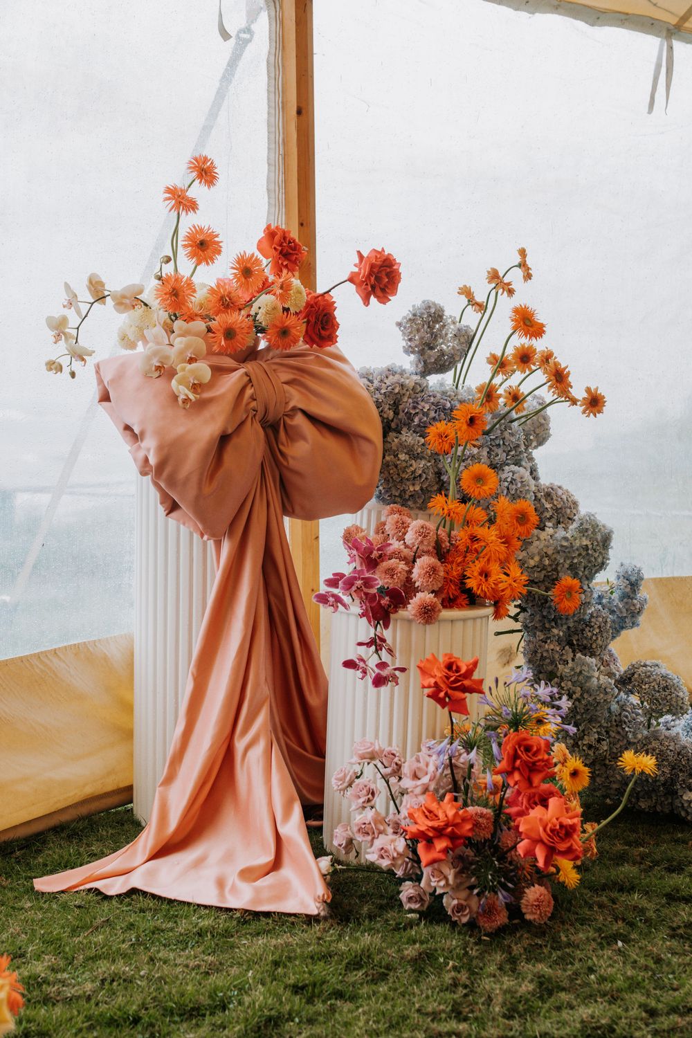 Elegant peach-colored drapes adorned with vibrant orange and pink floral arrangements create a romantic outdoor setting.