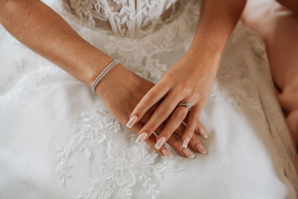 Close-up view of hands delicately touching white lace fabric with elegant wedding ring details.