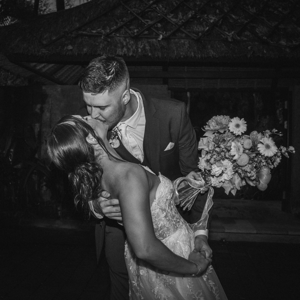 A romantic black and white photograph captures newlyweds sharing a passionate dip kiss during their wedding reception.