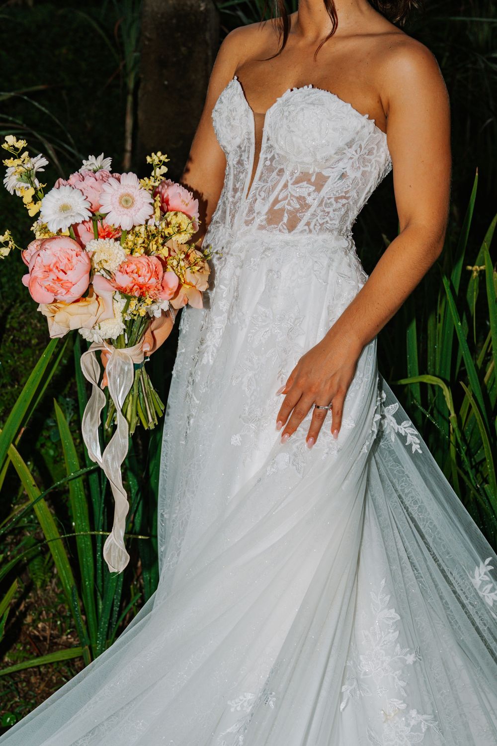Wedding dress detail showing intricate lace bodice and flowing tulle skirt with peach and pink floral bouquet.