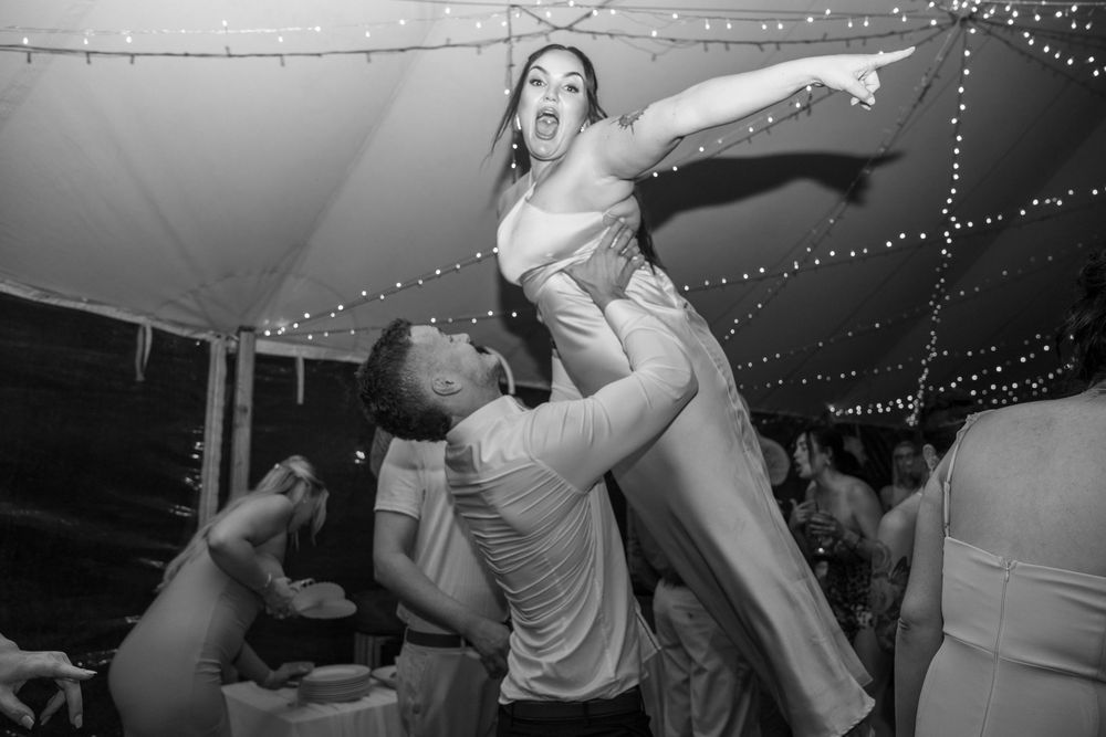 Several couples dance under string lights at an outdoor wedding celebration.