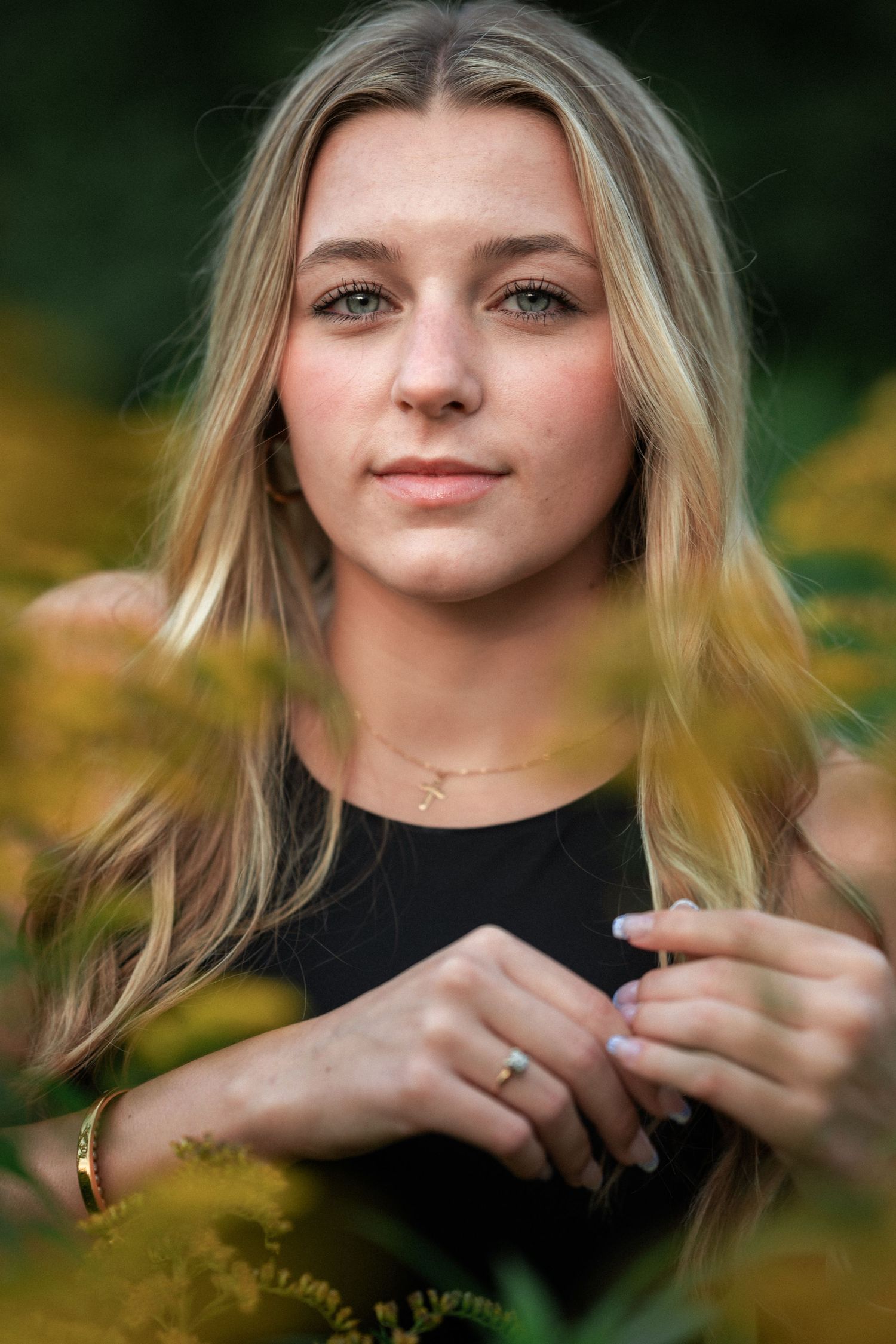 A blonde teenage girl with green eyes poses among golden autumn leaves outdoors.