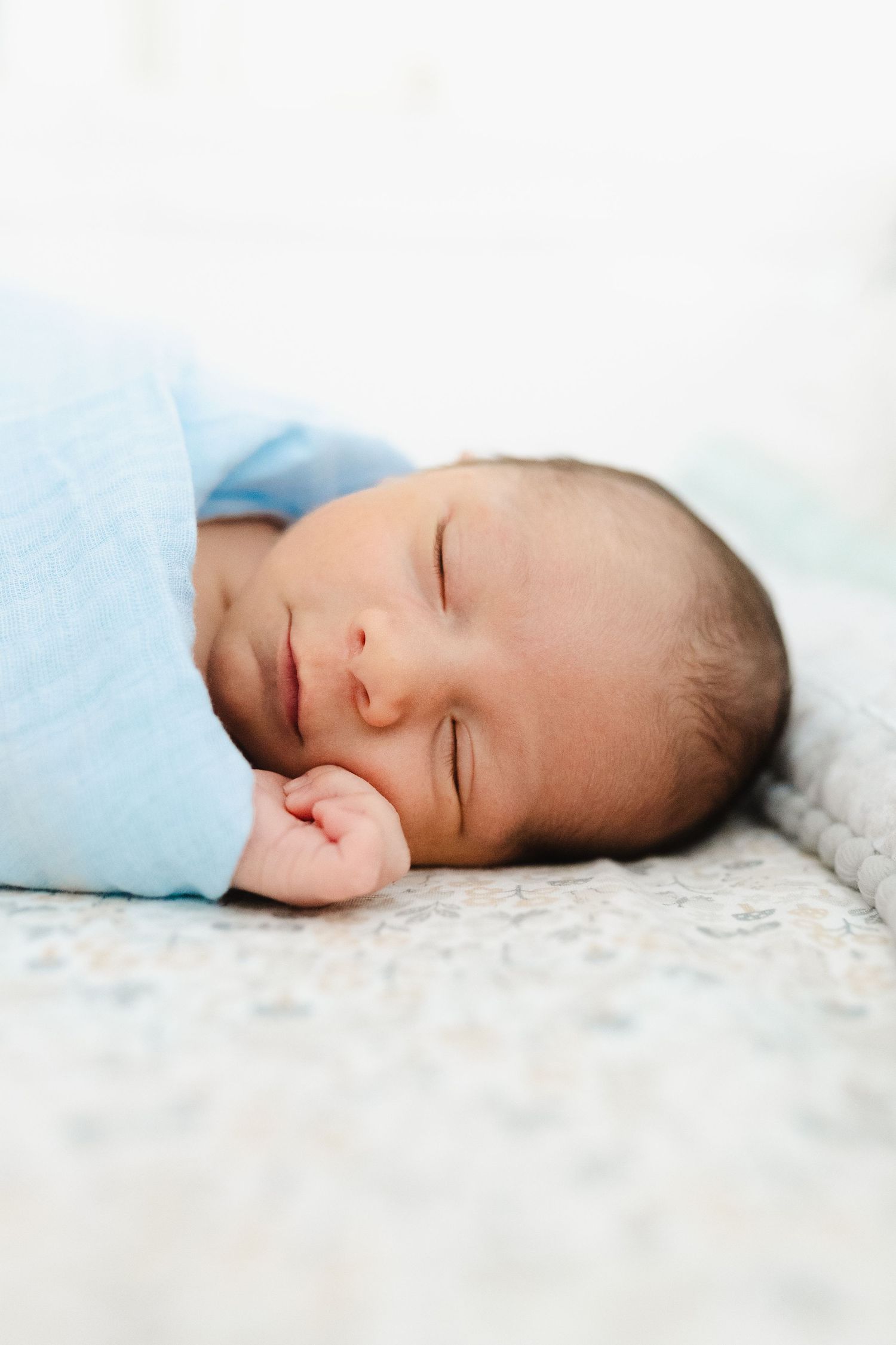 Peaceful sleeping baby wrapped in soft blue blanket on textured white surface.