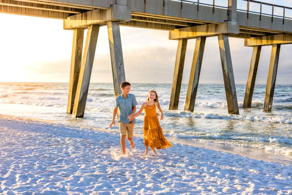 A couple strolls together on the beach near a wooden pier during sunset with waves rolling in.
