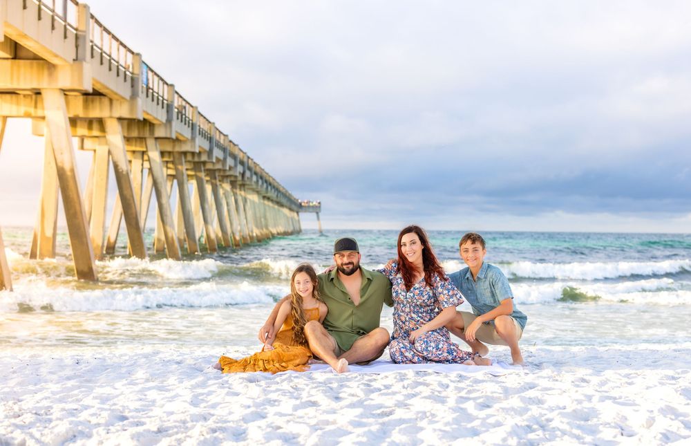 Beach scene at sunset with pier in background as group poses on white sand by ocean waves.