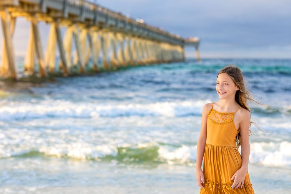 A bright mustard dress contrasts against the blue ocean waves and pier on a sunny beach day.