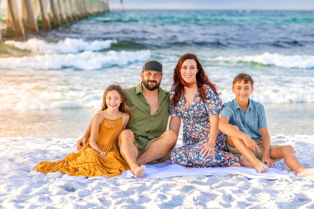 A group relaxes together on a sandy beach with ocean waves and blue sky in the background. Sea Glass Photography of Navarre Florida