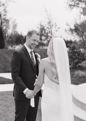 Black and white photo of a smiling groom holding his bride's hands during a romantic wedding first look outdoors.
