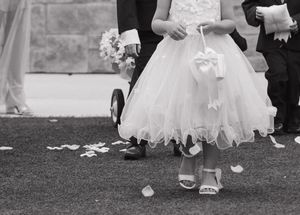 Flower girl in white dress scattering petals at a wedding ceremony, captured in black and white.