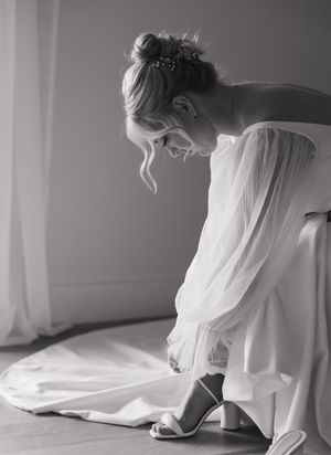 A flowing white wedding dress train cascades gracefully across a light-colored floor in black and white photography.