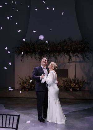 A couple dances together at an evening wedding reception as rose petals fall around them.