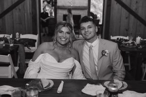 Black and white photo of a bride and groom sitting together at their rustic barn wedding reception.