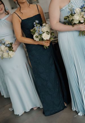 Bridesmaids in light blue and dark navy gowns holding white and blue floral bouquets at a wedding.