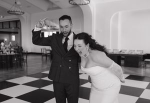 Bride and groom share a joyful first dance on a black and white checkered floor at their wedding reception.