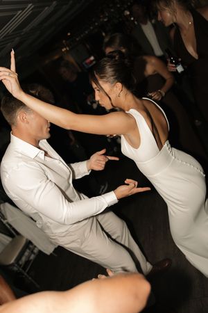 People in white outfits dance energetically at a dark club or party venue.