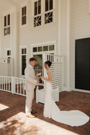 A bride and groom share an intimate moment on a white porch with brick flooring during their elegant wedding ceremony.
